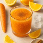 Chilled carrot citrus drink with shredded carrots, lemon and orange slices, ice cubes, and cinnamon in a clear glass.